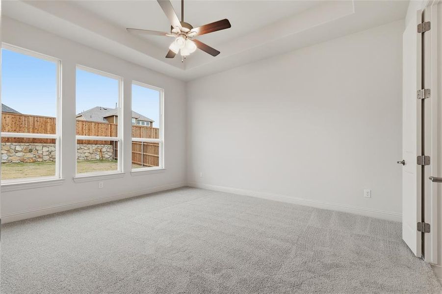 Empty room with a raised ceiling, light carpet, and ceiling fan