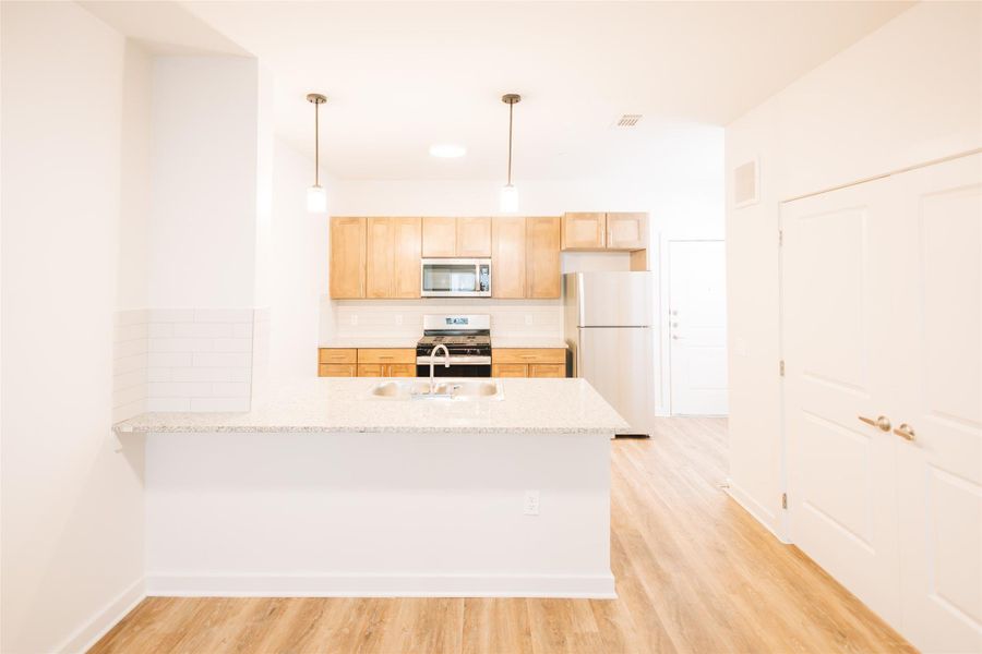 Kitchen with appliances with stainless steel finishes, a peninsula, a sink, backsplash, and light wood-style flooring