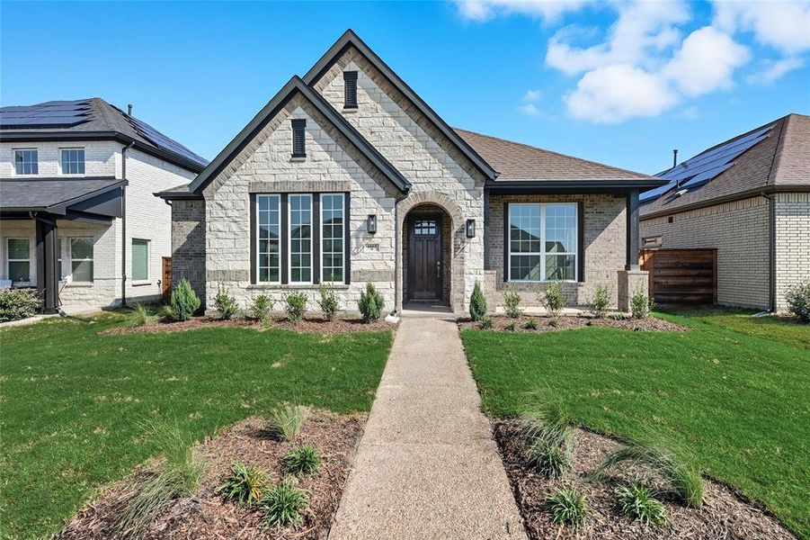 French country inspired facade with stone siding, a front lawn, and brick siding