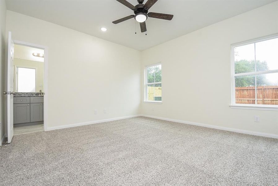 2nd floor gameroom with beige walls, carpeted floor, ceiling fan, window with view of a fence, and doorway leading to a bathroom with vanity.