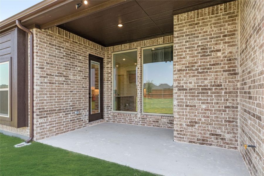 Covered back patio with brick exterior, concrete floor, and sliding glass door leading inside