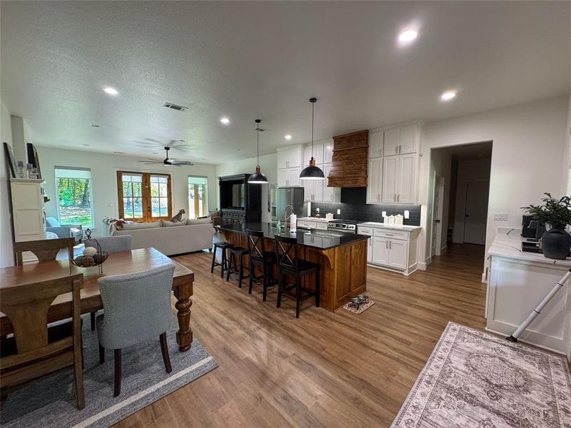 Kitchen featuring custom exhaust hood, a ceiling fan, a kitchen island with sink, pendant lighting, and light wood finished floors Kitchen featuring custom exhaust hood, a ceiling fan, a kitchen island with sink, pendant lighting, and light wood finished floors