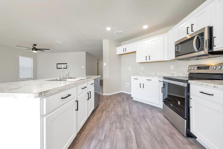 Kitchen with white cabinetry, sink, ceiling fan, appliances with stainless steel finishes, and a center island with sink