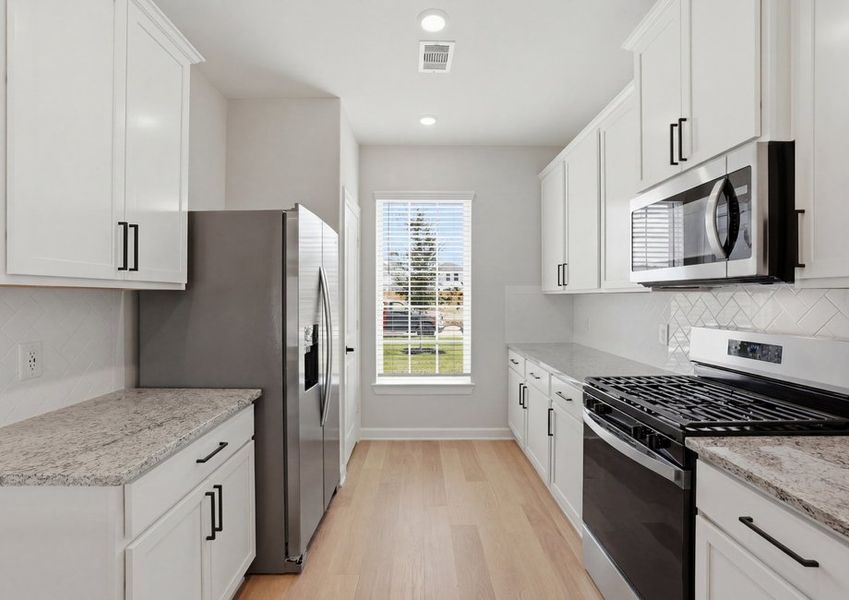 Kitchen featuring white cabinetry, a stainless refrigerator and microwave, and granite countertops.