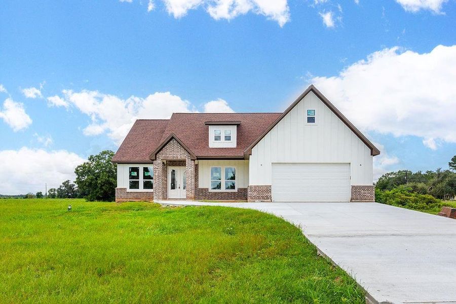 Charming modern farmhouse with a spacious driveway, featuring a blend of brick and siding, set amidst a lush green landscape. Charming modern farmhouse with a spacious driveway, featuring a blend of brick and siding, set amidst a lush green landscape.