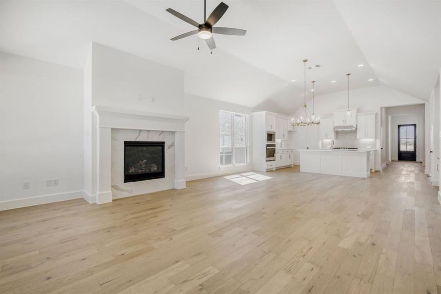 Unfurnished living room with suspended lighting, light wood-style flooring, ceiling fan, a high end fireplace, and lofted ceiling