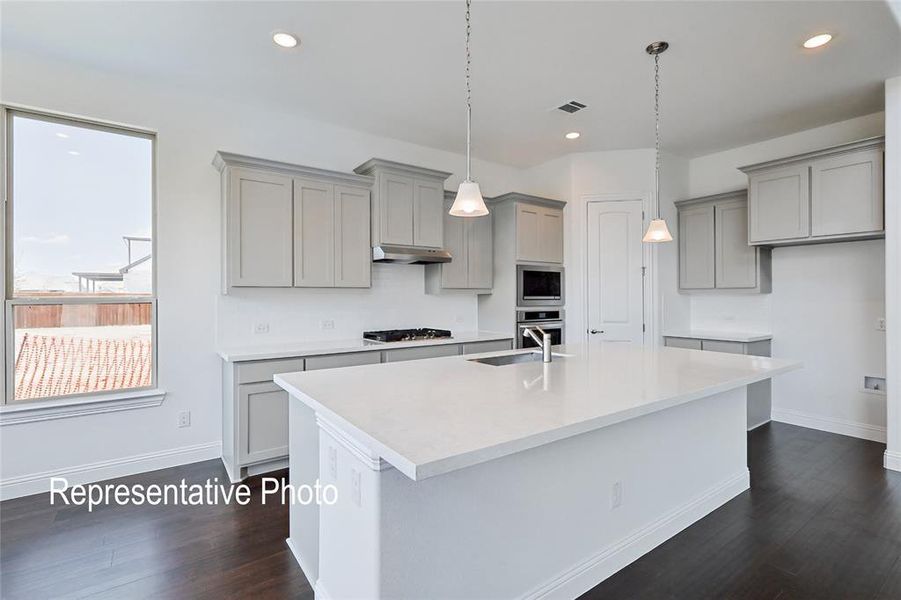 Modern kitchen featuring light gray cabinetry with crown molding, a large central island with a white solid surface countertop, and stainless steel built-in appliances