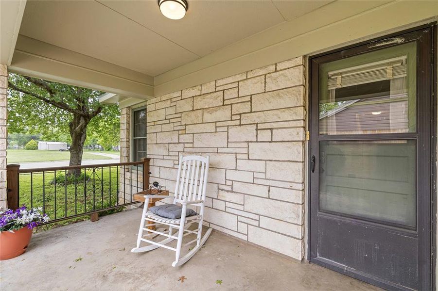 Stone veneer facade with a covered concrete porch, featuring a dark metal entry door and decorative railing with wood posts Stone veneer facade with a covered concrete porch, featuring a dark metal entry door and decorative railing with wood posts