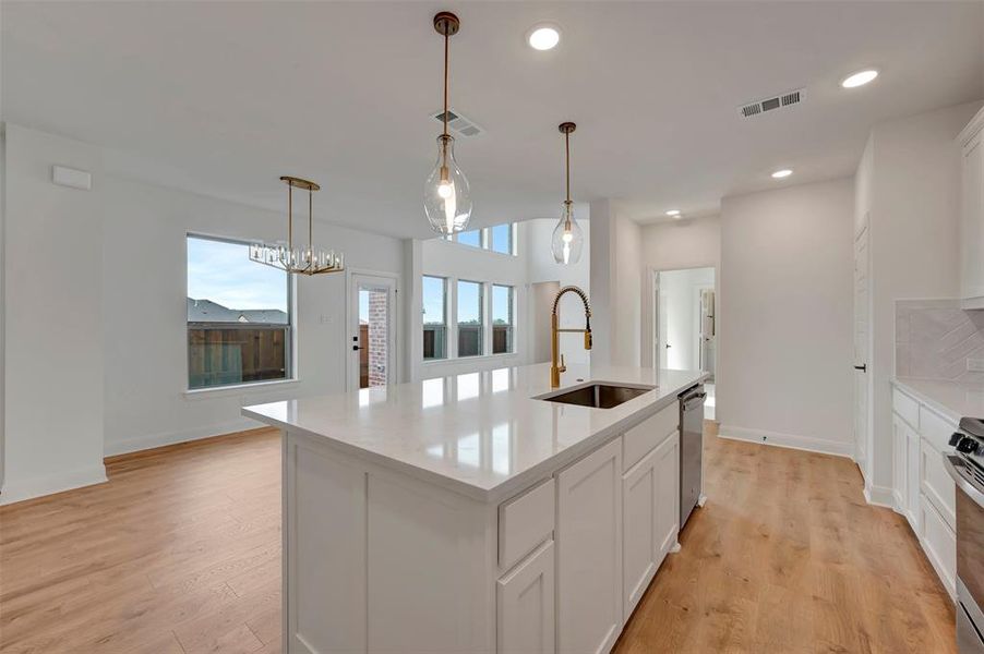 Kitchen with a center island with sink, white cabinets, light wood-style floors, light stone countertops, and pendant lighting