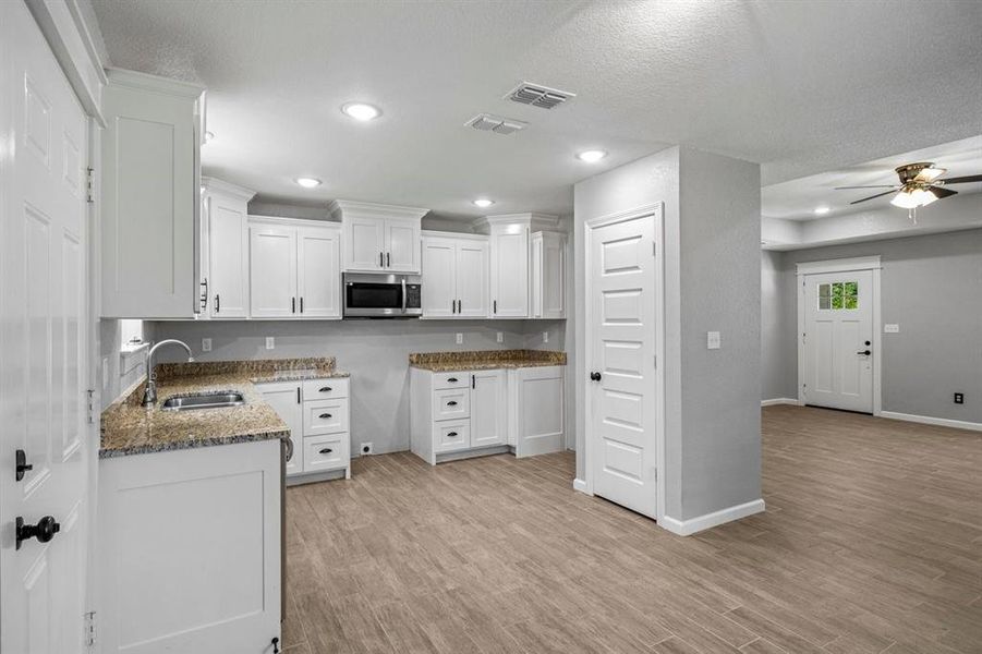 Kitchen featuring white cabinets, dark stone counters, stainless steel microwave, ceiling fan, and a textured ceiling Kitchen featuring white cabinets, dark stone counters, stainless steel microwave, ceiling fan, and a textured ceiling
