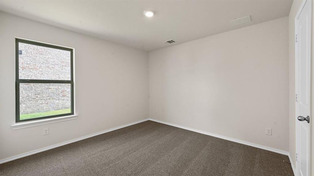 Carpeted interior room featuring a double-hung window with dark trim, neutral wall paint, and a white interior door with a dark handle Carpeted interior room featuring a double-hung window with dark trim, neutral wall paint, and a white interior door with a dark handle