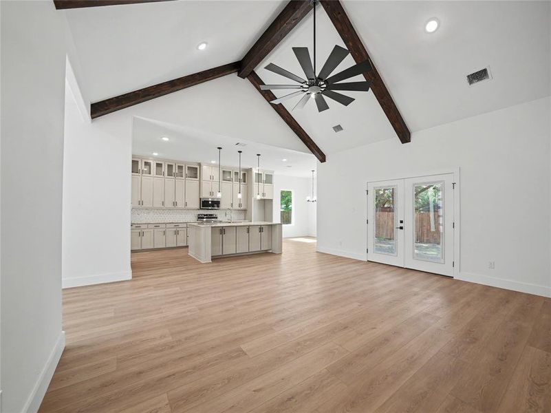 Expansive living area featuring vaulted ceilings with exposed wood beams, a modern ceiling fan, and light wood-finish flooring Expansive living area featuring vaulted ceilings with exposed wood beams, a modern ceiling fan, and light wood-finish flooring