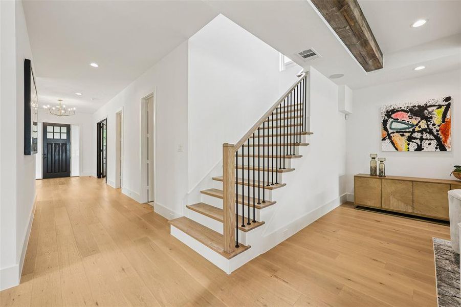Foyer featuring wood-finish flooring, a modern staircase with dark balusters, recessed lighting, and a prominent wood ceiling beam