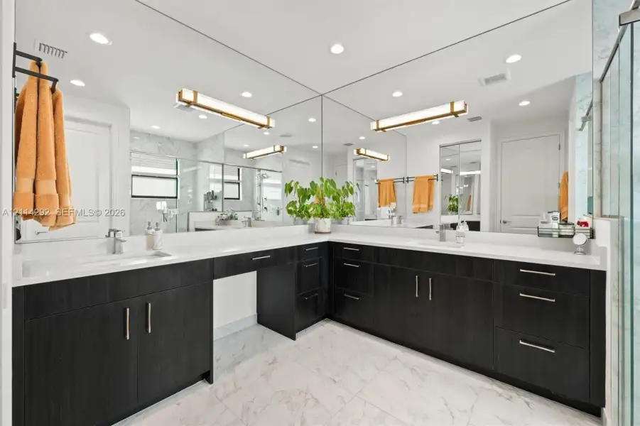 Dual-sink vanity with dark wood-finish cabinetry, solid surface countertops, polished metal hardware, and full-wall mirrors