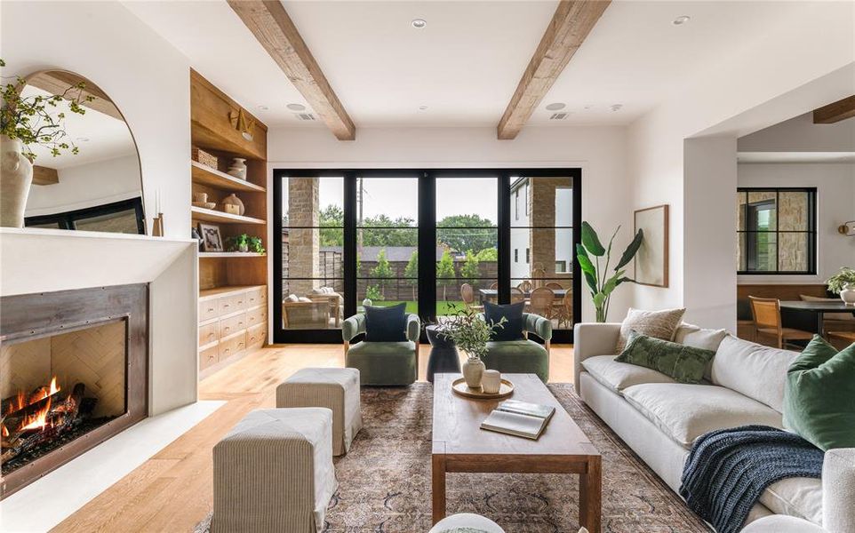 Living room with light wood-style flooring, a lit fireplace, and beamed ceiling