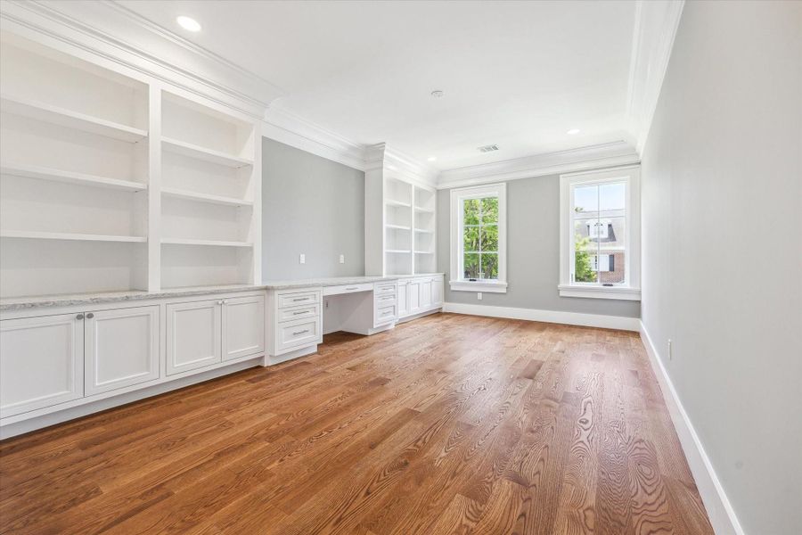 Another view of this secondary bedroom that features hardwood floors, built-in white cabinetry with ample shelving, and two large windows that offer plenty of natural light.   There is a walk-in closet and an en-suite bath.  This could also be ideal for a home office or library.