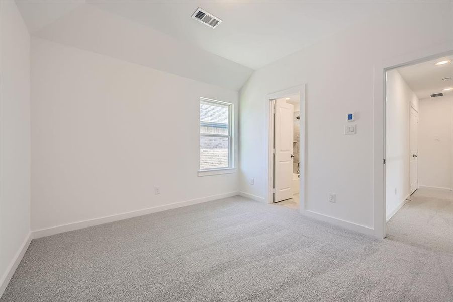 Unfurnished bedroom with light carpet, baseboards, lofted ceiling, and ensuite bathroom Unfurnished bedroom with light carpet, baseboards, lofted ceiling, and ensuite bathroom