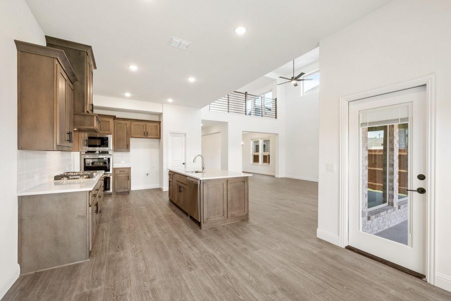 Open kitchen with brown wood cabinets, center island, stainless appliances, and wood-look floors in a high-ceiling home