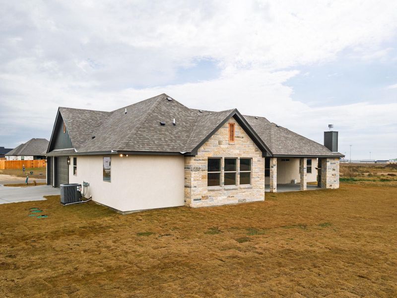 Back of house featuring a patio area, concrete driveway, a lawn, stone siding, and a garage