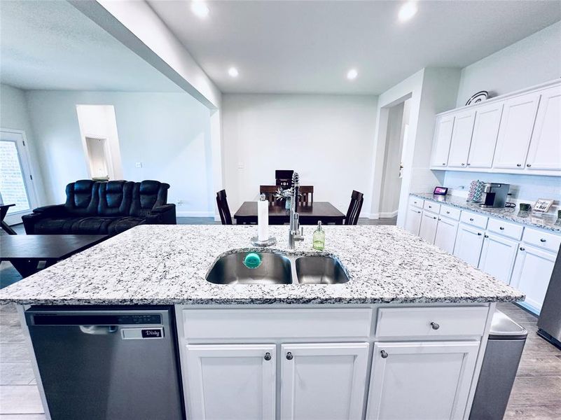 Kitchen featuring sink, light hardwood / wood-style floors, stainless steel dishwasher, light stone countertops, and white cabinetry