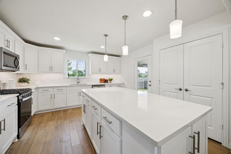 The light and bright kitchen will make your cook's heart sing! The kitchen features quartz countertops, hexagonal tile backsplash, pendant lights and white cabinetry with soft close - all upgrades from the standard builder package! Through the double doors is a spacious pantry. The glass door leads to the amazing back patio.