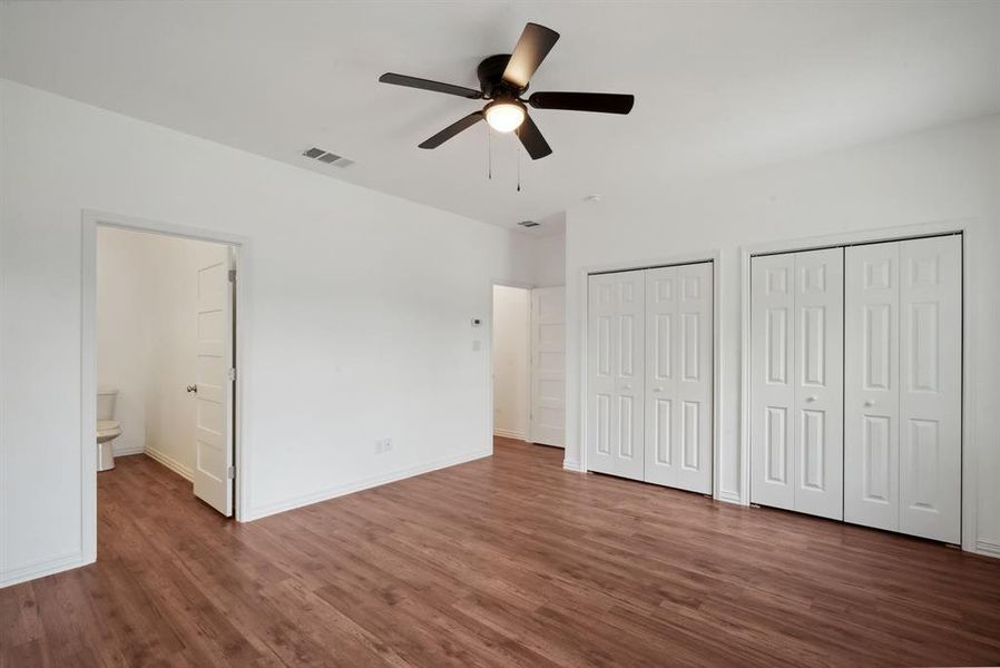 Unfurnished bedroom with connected bathroom, multiple closets, ceiling fan, and dark hardwood / wood-style floors