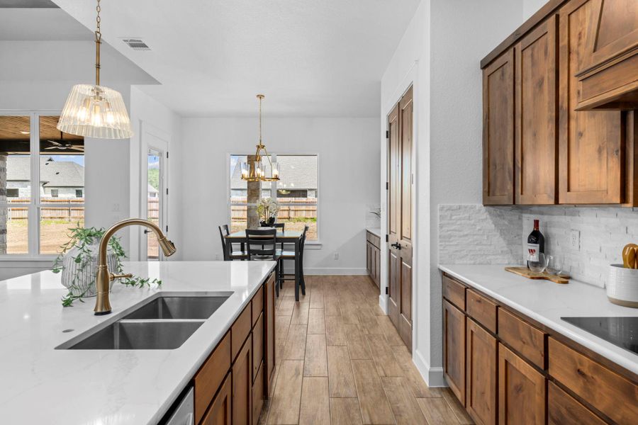 Kitchen featuring wood finish floors, suspended lighting, tasteful backsplash, wood finish cabinets, and light stone countertops