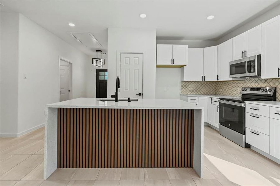 Kitchen with appliances with stainless steel finishes, an island with sink, light countertops, decorative backsplash, and white cabinetry