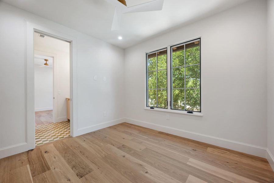 Natural light pours through multipane windows onto rich hardwood floors in this pristine bedroom.