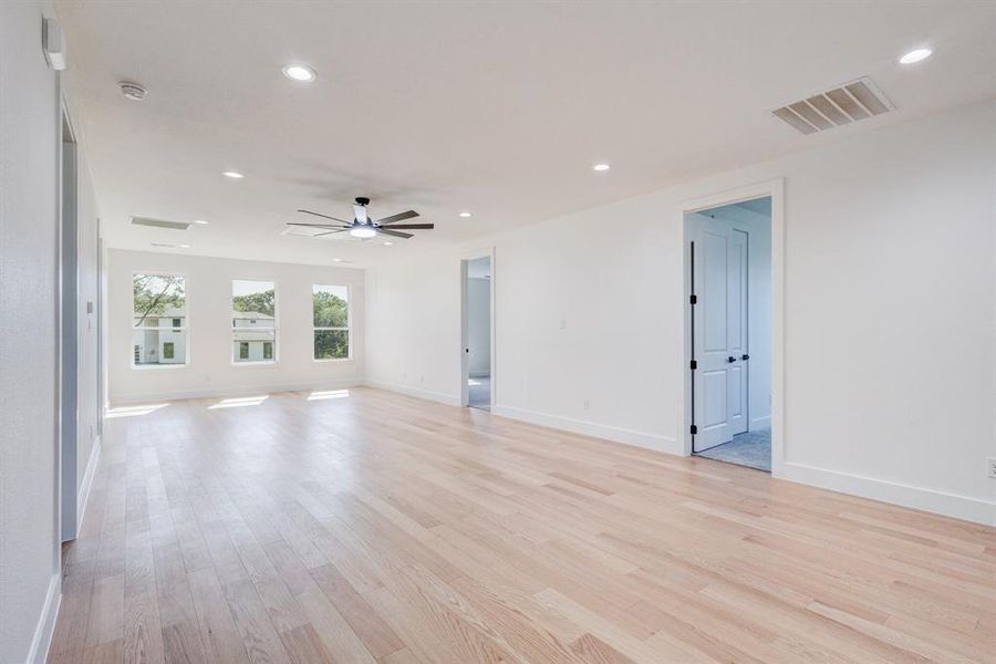 Spacious room featuring light wood-finish flooring, recessed lighting, and a contemporary ceiling fan Spacious room featuring light wood-finish flooring, recessed lighting, and a contemporary ceiling fan