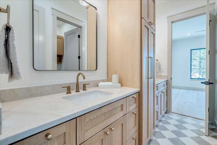 A well-appointed vanity with warm wood cabinetry, elegant gold hardware, and checkerboard floor tiles.