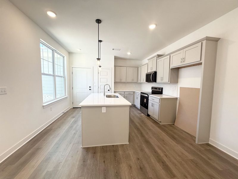 Kitchen with stainless steel appliances, a kitchen island with sink, decorative backsplash, dark wood-style flooring, and decorative light fixtures