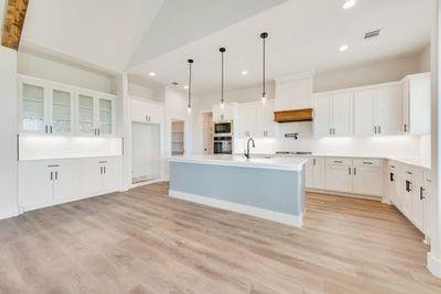 Kitchen featuring a kitchen island with sink, pendant lighting, white cabinetry, and light hardwood / wood-style floors