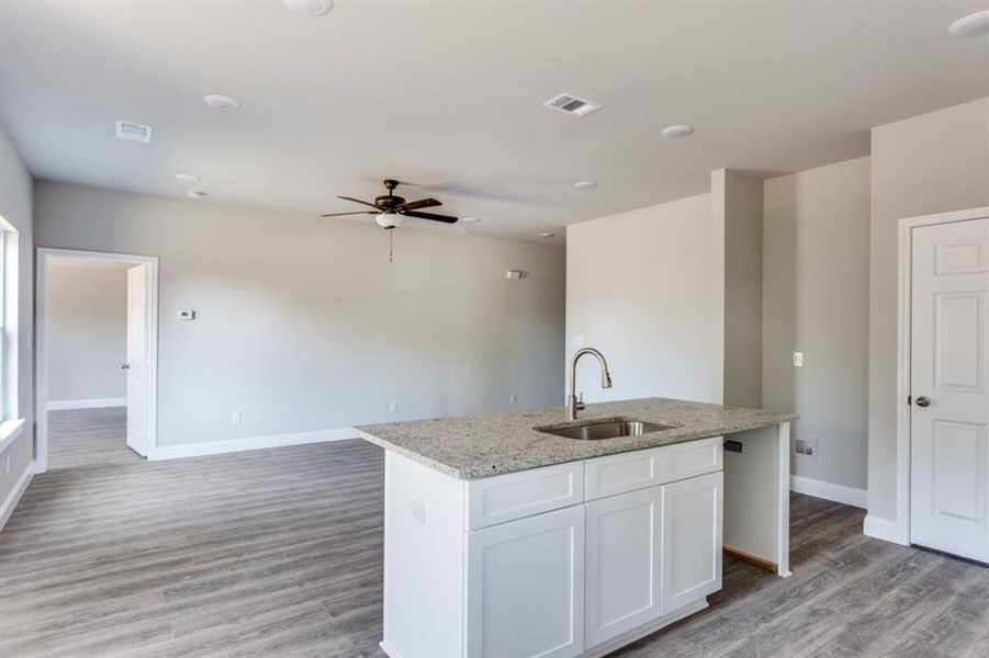 Kitchen featuring white cabinetry, light stone countertops, a center island with sink, light wood finished floors, and open floor plan