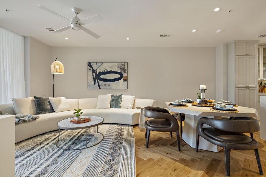 An inviting open-concept living and dining area features warm wood flooring and recessed ceiling lights.