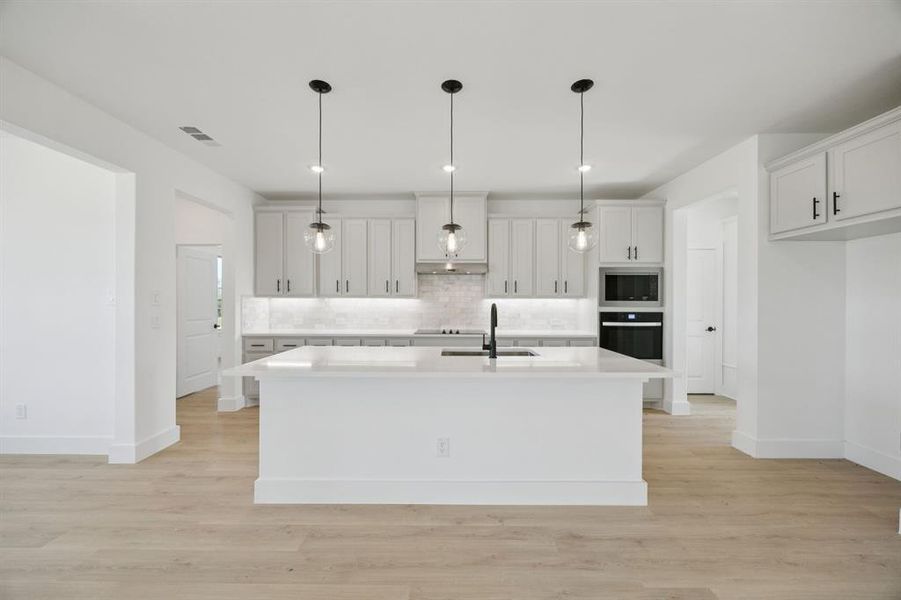 Kitchen with hanging light fixtures, backsplash, light wood-type flooring, a kitchen island with sink, and recessed lighting Kitchen with hanging light fixtures, backsplash, light wood-type flooring, a kitchen island with sink, and recessed lighting