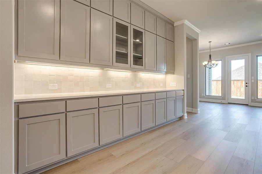 Kitchen with tasteful backsplash, light hardwood / wood-style floors, gray cabinets, and ornamental molding