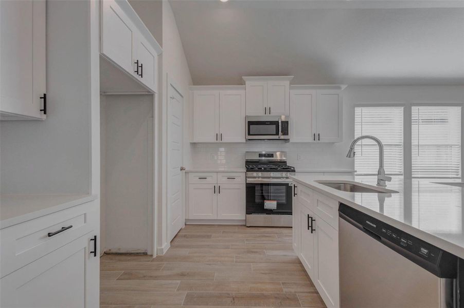 A modern chef’s kitchen awaits with sleek quartz countertops, stainless appliances, and crisp shaker cabinetry. The oversized island with deep sink and pull-down faucet provides prep space and bar seating, while the walk-in pantry and ample storage make daily living both efficient and elegant.