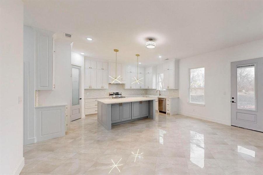 Kitchen featuring gray cabinets, decorative light fixtures, backsplash, stainless steel appliances, and a kitchen island