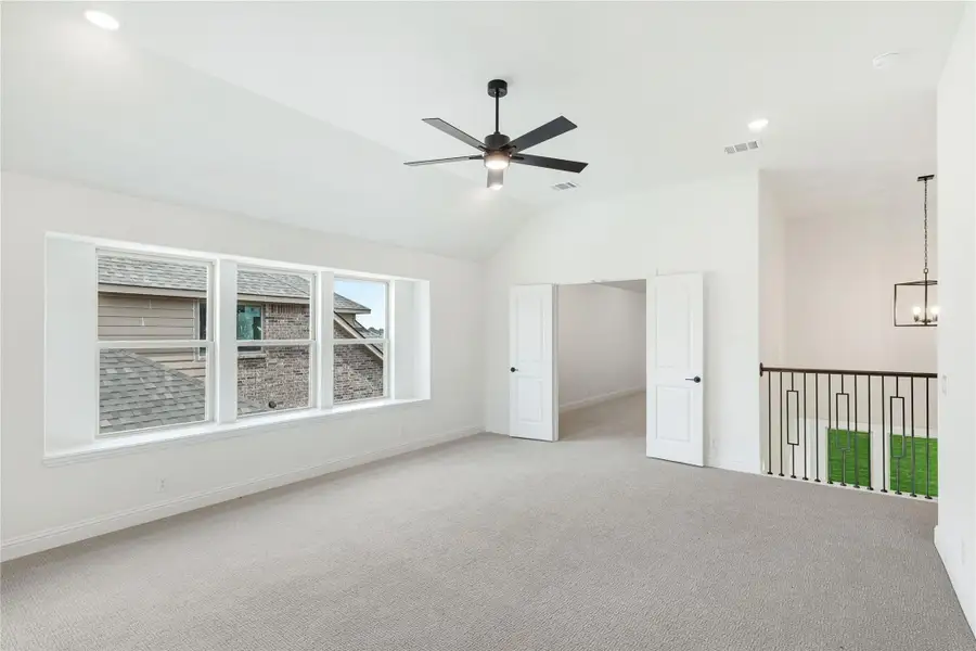 Spacious bedroom with vaulted ceiling, ceiling fan, carpet flooring, and large windows overlooking neighboring homes