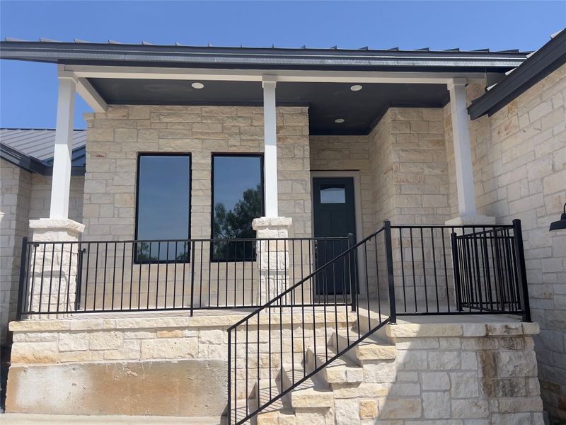 A welcoming stone facade with a covered entry, featuring a sleek metal roof and modern black railing.