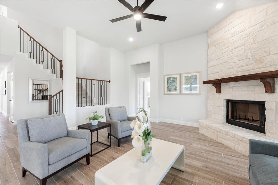 Living room with floor-to-ceiling stone fireplace, ceiling fan, gray seating, and staircase with metal balusters Living room with floor-to-ceiling stone fireplace, ceiling fan, gray seating, and staircase with metal balusters
