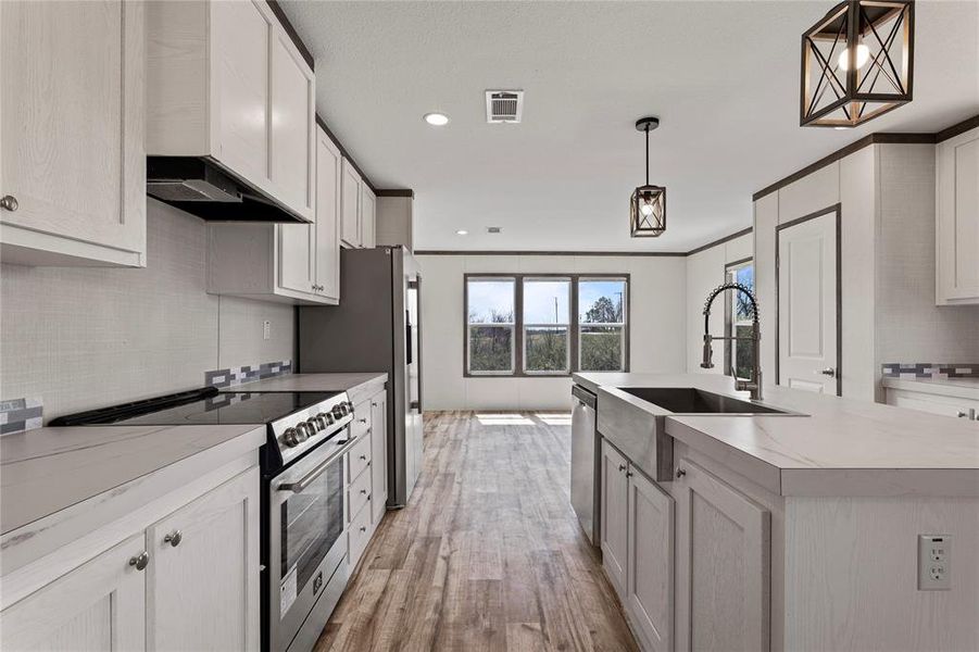 Kitchen featuring stainless steel appliances, light countertops, pendant lighting, light wood finished floors, and a kitchen island with sink