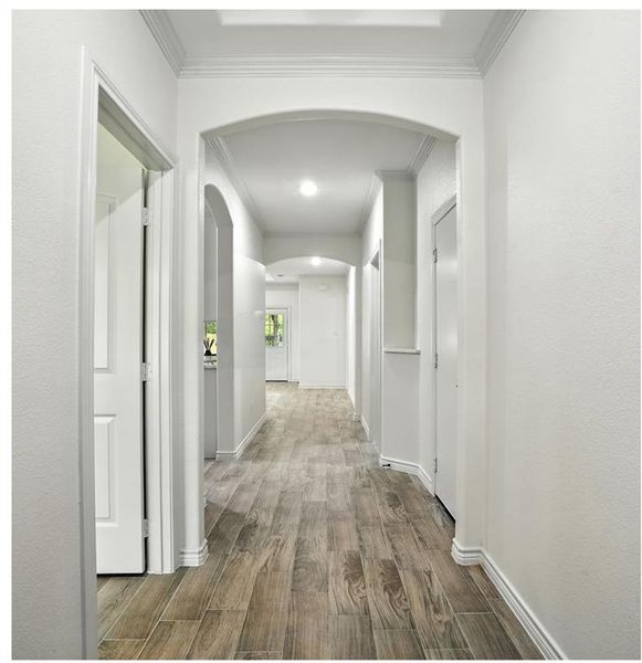 Hallway featuring arched walkways, wood finished floors, and crown molding