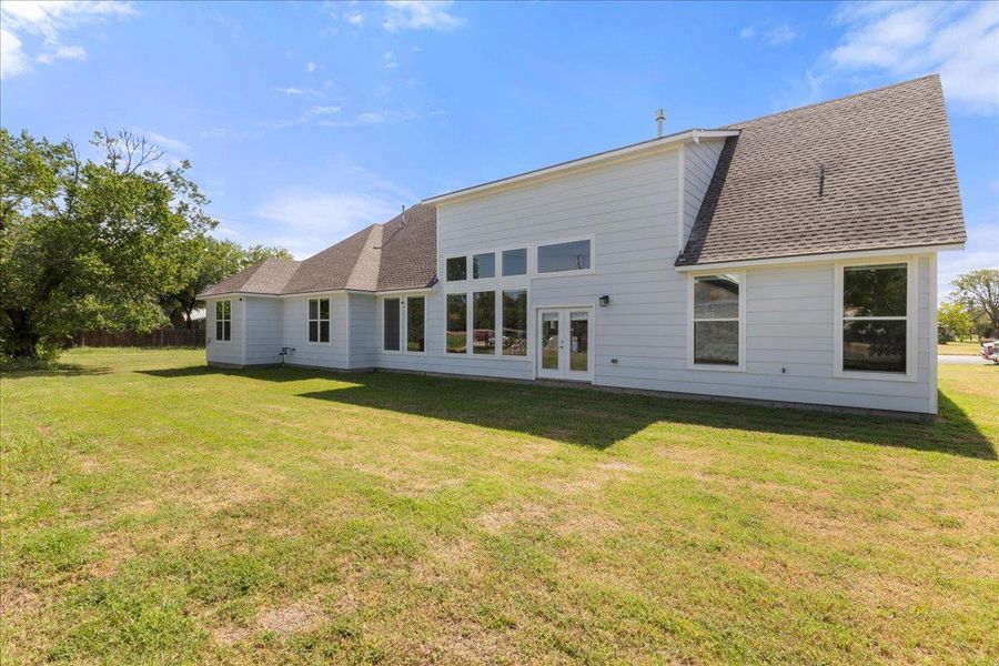 Back of property featuring french doors, a shingled roof, and a lawn Back of property featuring french doors, a shingled roof, and a lawn