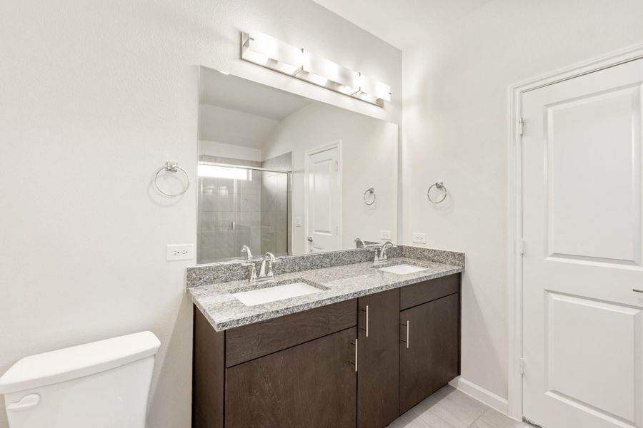 Bathroom with double sink vanity, dark wood cabinets, granite countertop, and large mirror with overhead lighting