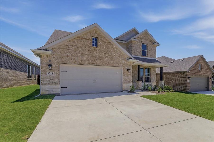 Brick exterior featuring stone accents, a covered entry, and an attached two-car garage