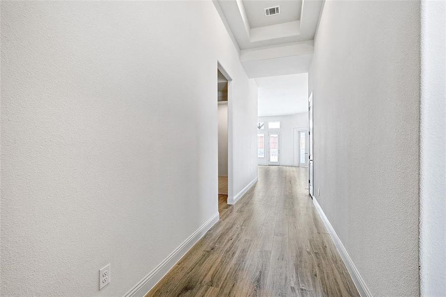 Hall with light wood-style flooring, a textured wall, and a raised ceiling