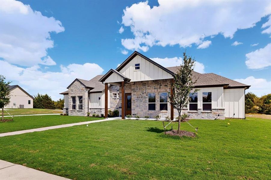 Modern farmhouse style home featuring board and batten siding, a front yard, and stone siding