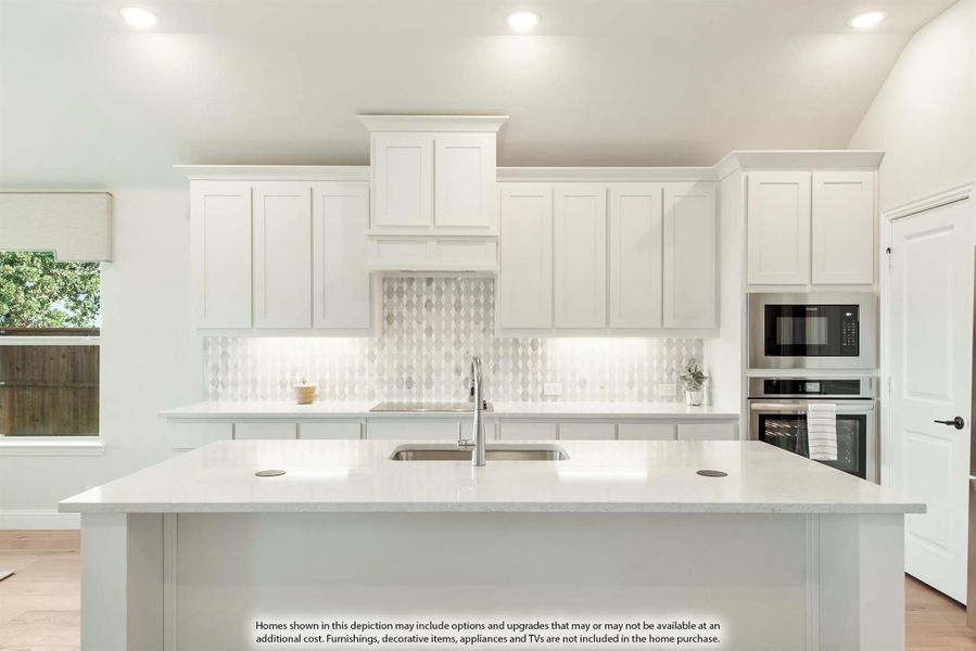 Kitchen with white cabinets, patterned tile backsplash, large island with sink, and built-in stainless steel appliances